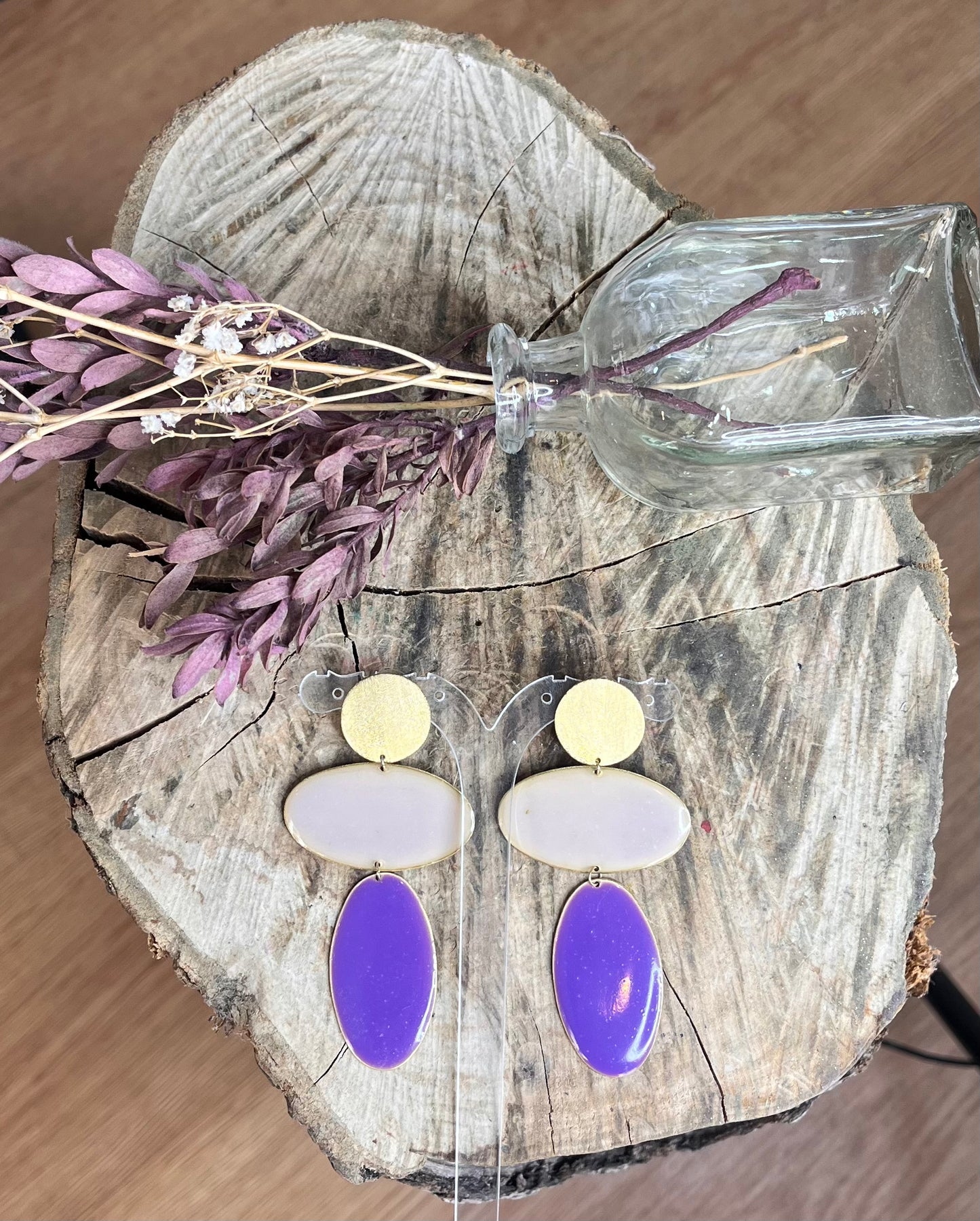 Pendientes maxicolor de aktual morados, sobre tronco y flores